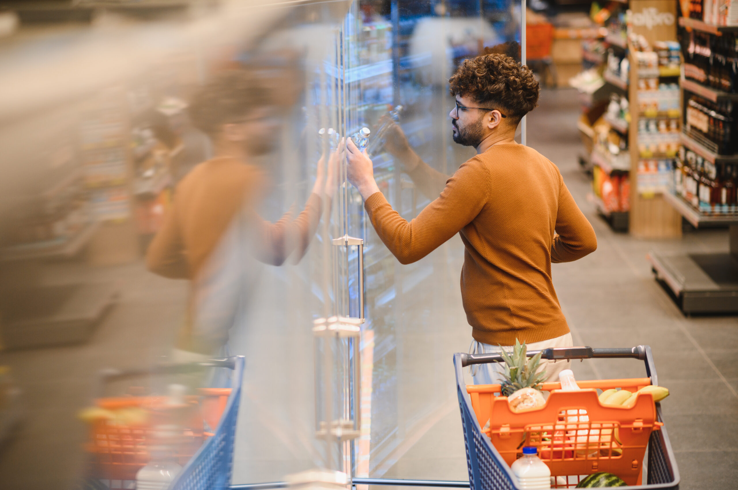 Arab man selecting groceries while opening the refrigerator door in a supermarket, engaging in a typical shopping experience