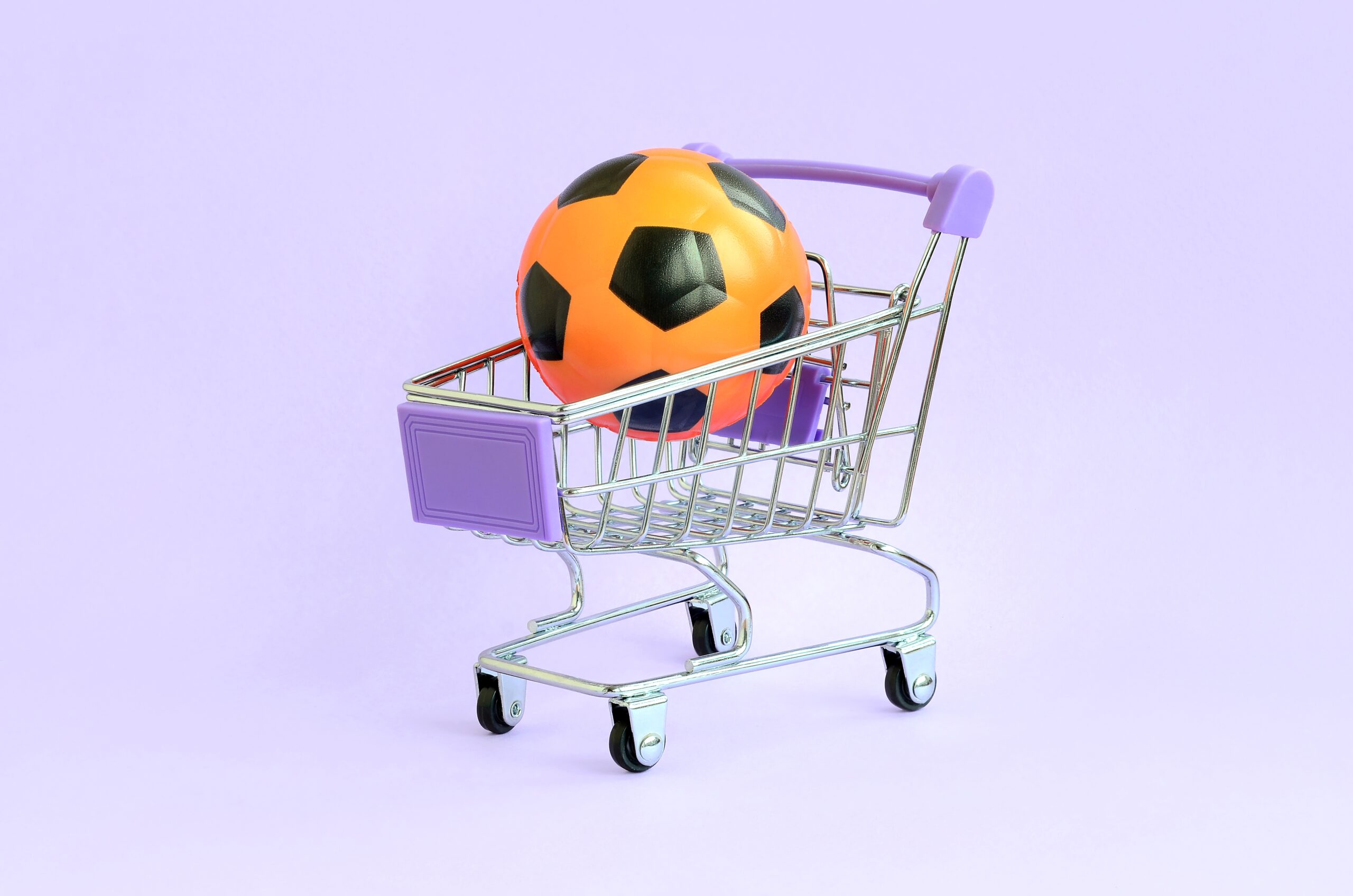 Balón naranja dentro de un pequeño carrito de compras sobre fondo morado